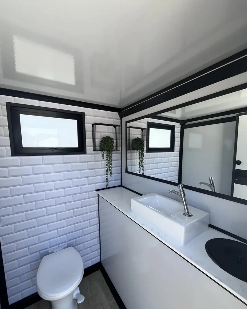 Restroom trailer stall interior with flushing toilet, vanity sink, mirror and window